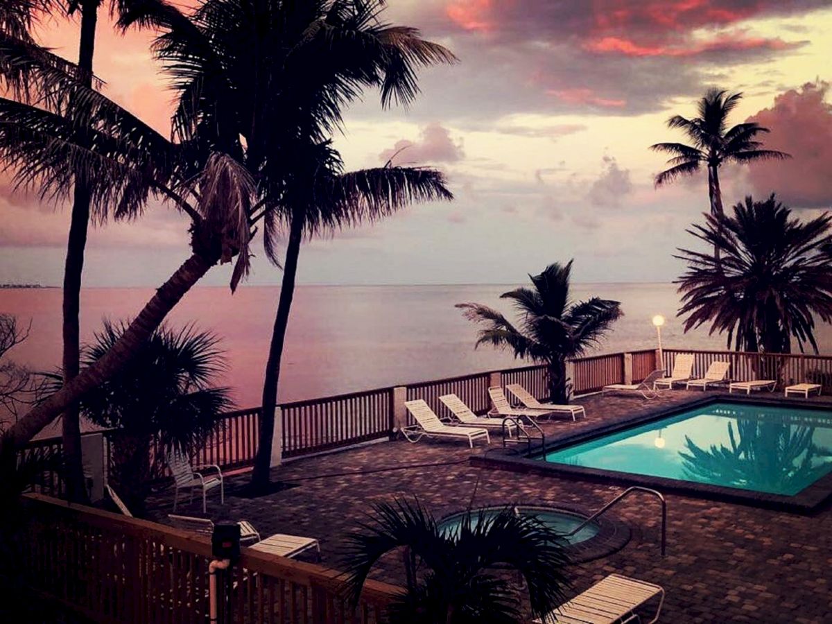 A serene sunset view by a pool with palm trees, lounge chairs, and a calm ocean in the background, creating a peaceful tropical ambiance.