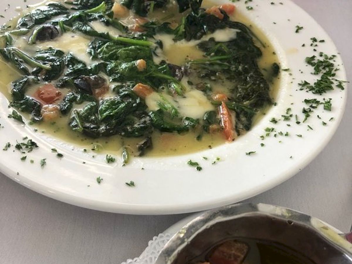 The image shows a plate of leafy greens in a creamy sauce, a small side dish with vegetables, and a piece of bread on another plate.