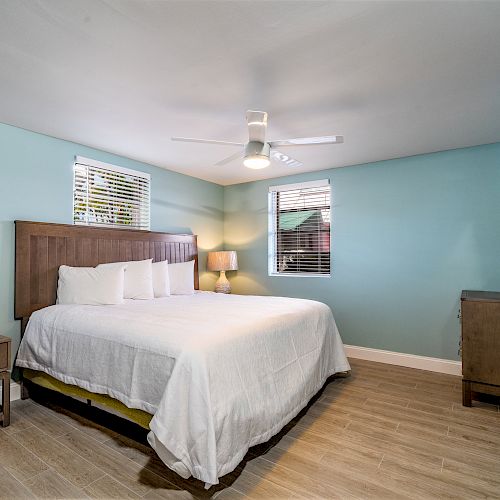 A bedroom with a large bed, bedside table, lamp, TV on the wall, and wooden flooring, against light blue walls.