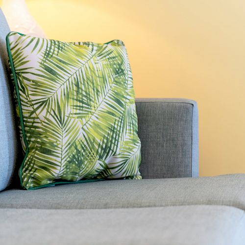 A light blue couch with a green leaf-patterned cushion against a yellow wall.