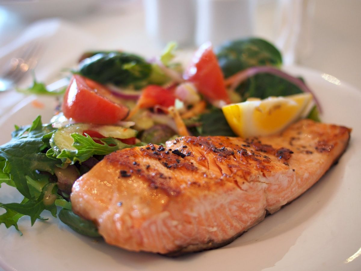 A plate with grilled salmon, mixed salad including tomatoes, red onions, and a lemon wedge.