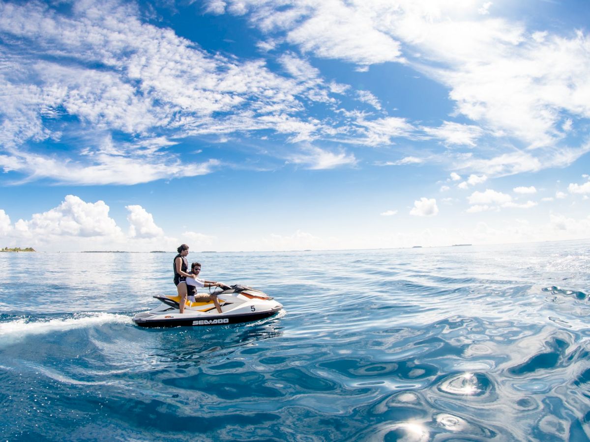 A person rides a jet ski on a calm, clear blue ocean under a bright sky with scattered clouds, creating a serene and adventurous scene.