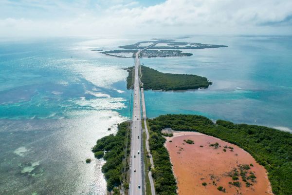 Aerial view of a scenic highway stretching over a series of islands with turquoise waters and greenery surrounding the area.