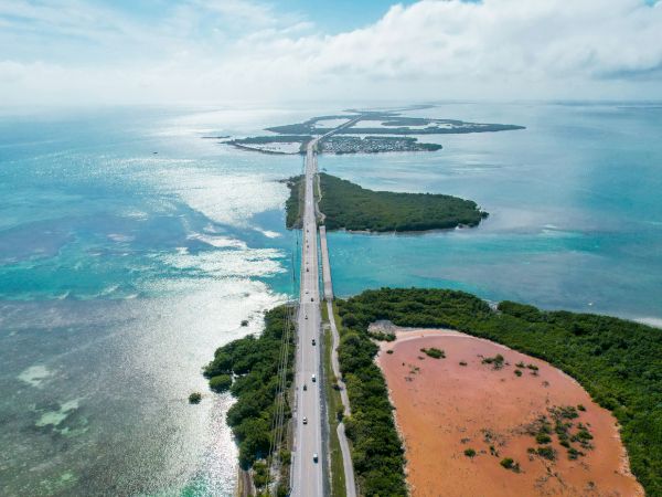 Aerial view of a scenic highway stretching over a series of islands with turquoise waters and greenery surrounding the area.