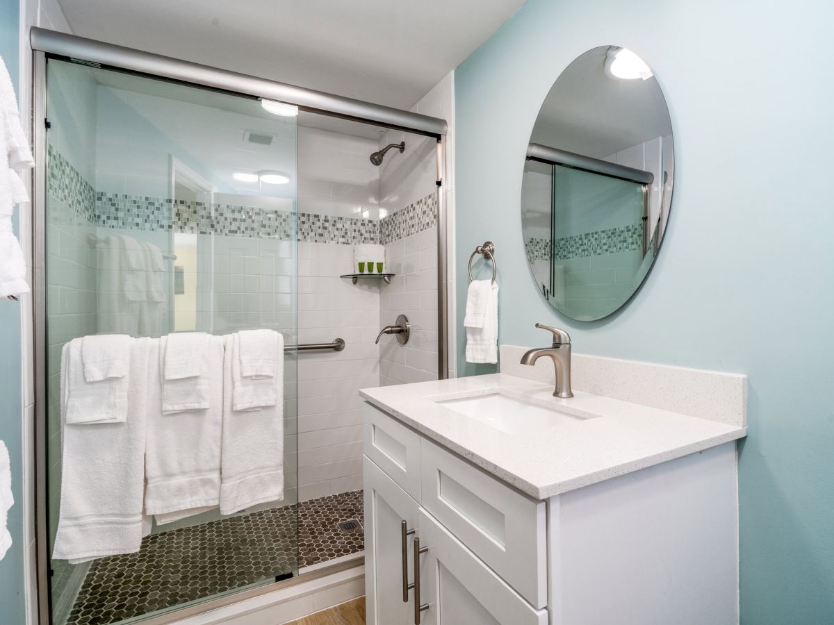 A modern bathroom with a glass shower, stacked white towels, a granite sink with faucet, and an arched mirror above.