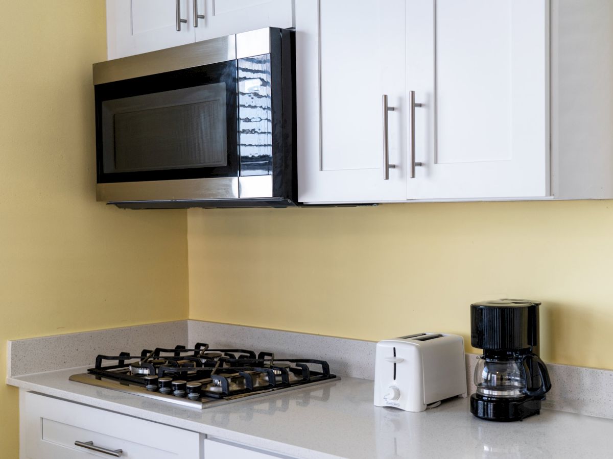 A kitchen counter with a stovetop, coffee maker, toaster, and built-in microwave beside white wall cabinets.