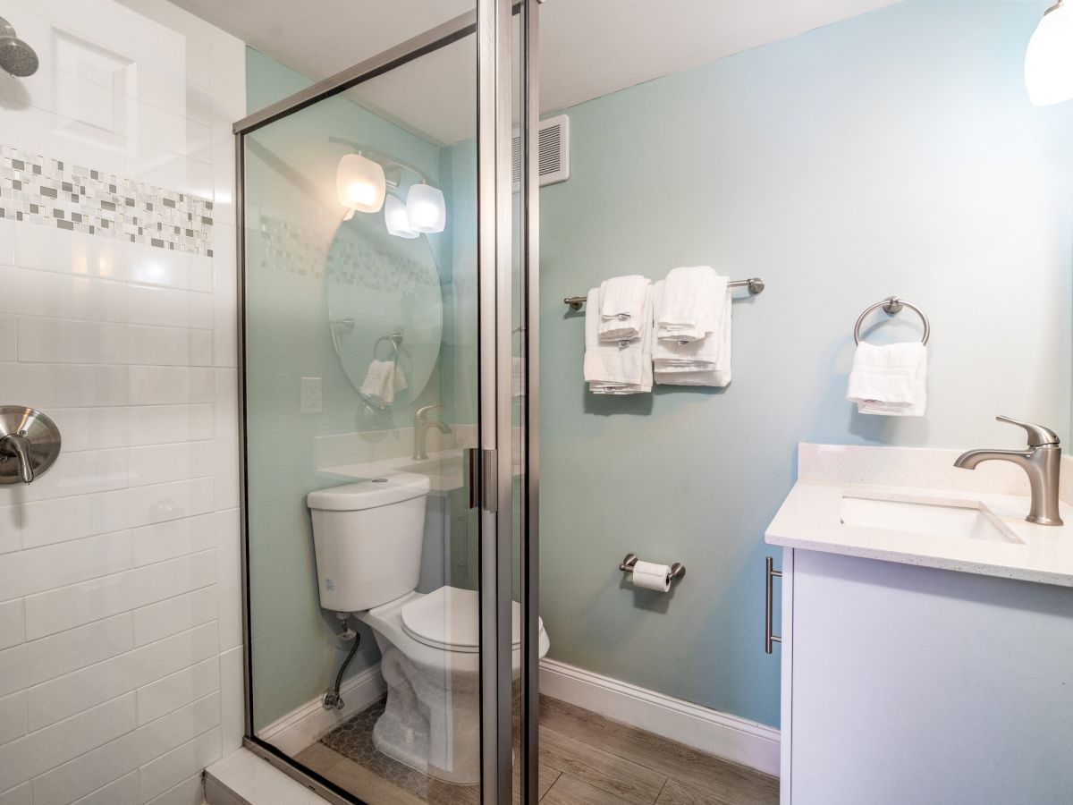 Bright bathroom with glass shower, toilet, sink, and neatly stacked white towels.