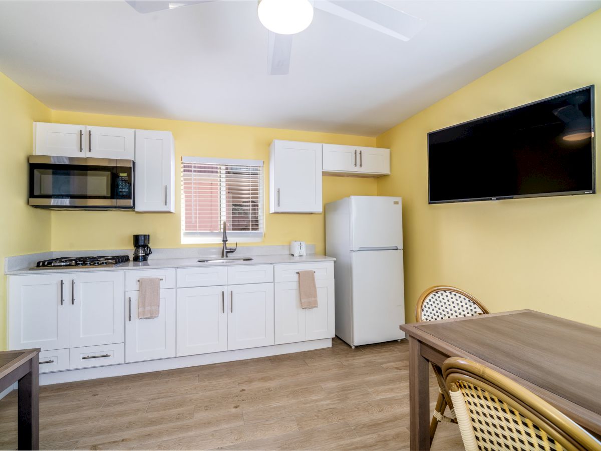Bright kitchen with white cabinets, microwave and stove, fridge, sink, and a wall TV, plus a small table by the doorway.