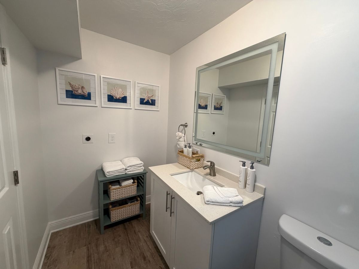 A bright bathroom with a white vanity, large mirror, faucet and soap, and framed seashell wall art.