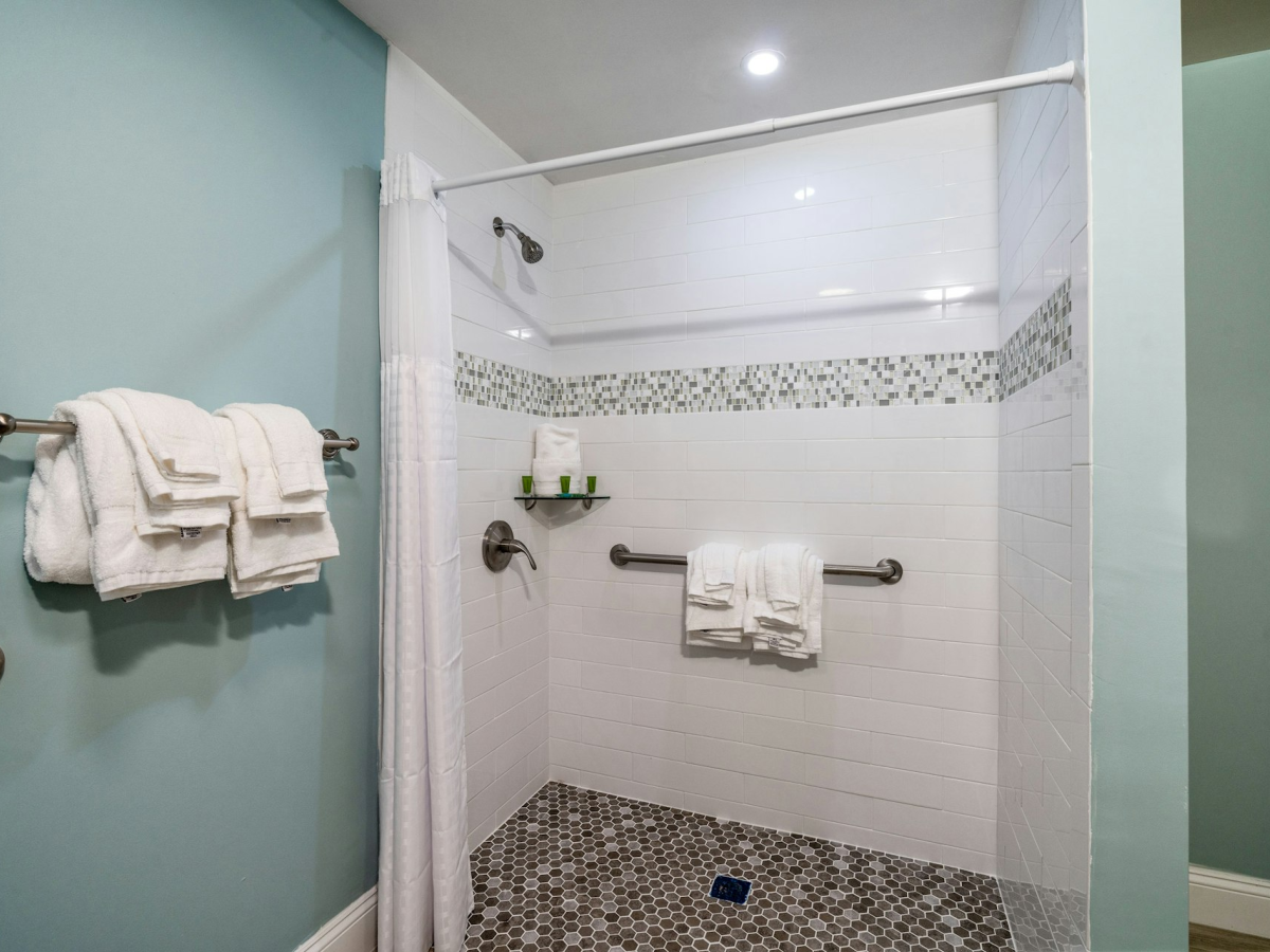 Clean tiled shower with a showerhead, chrome bars, stacked towels, and a mosaic accent border.