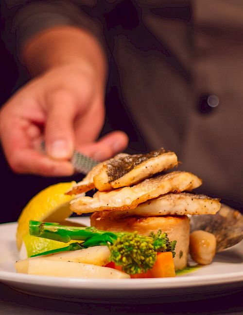 Chef plating a dish&mdash;grilled chicken/shrimp piled on vegetables on a plate, with a knife nearby.