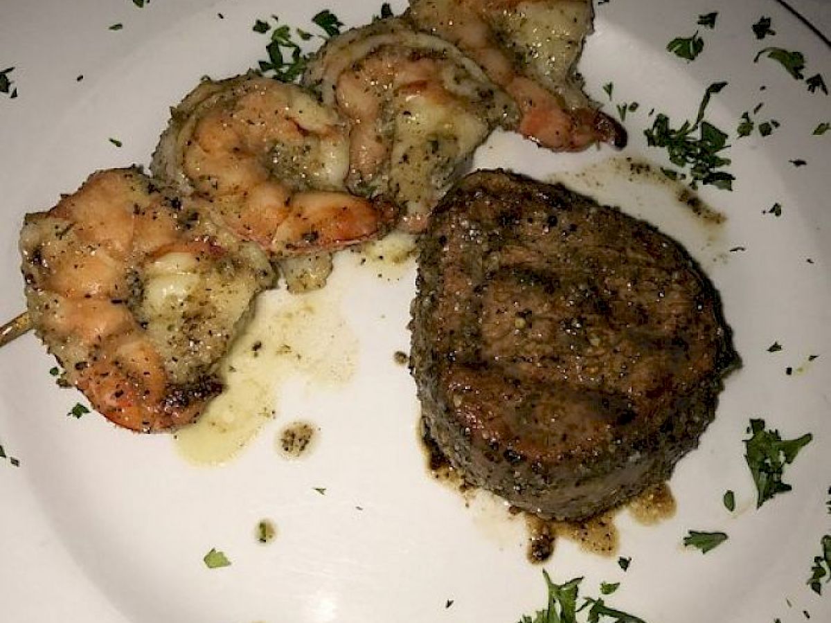 A plate with grilled shrimp and a filet mignon, garnished with chopped fresh herbs and some melted butter or sauce.